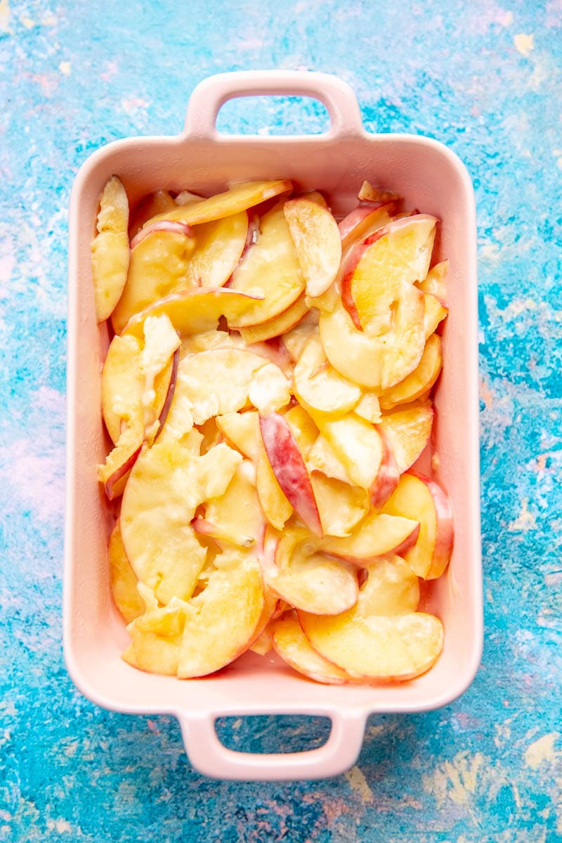 pink casserole dish with peaches tossed with condensed milk