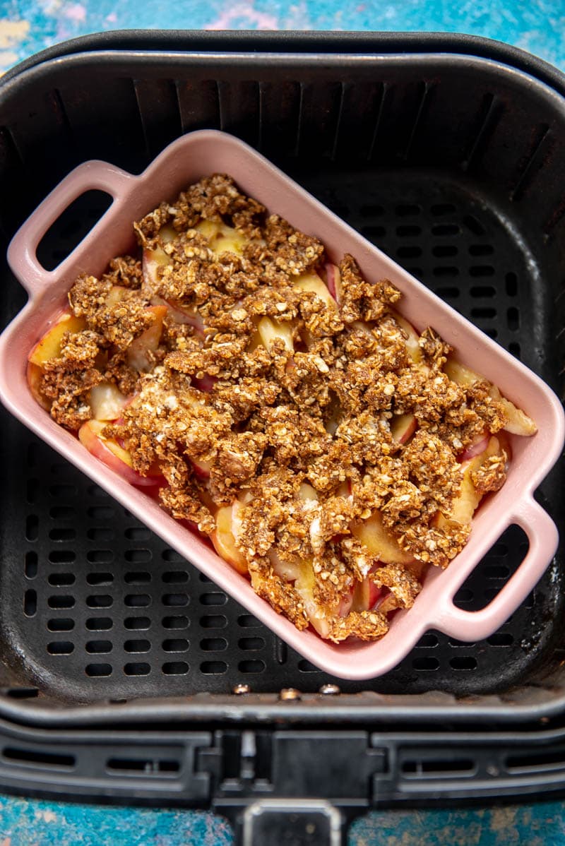 ready to cook peaches with crumbly topping in pink casserole dish inside air fryer basket