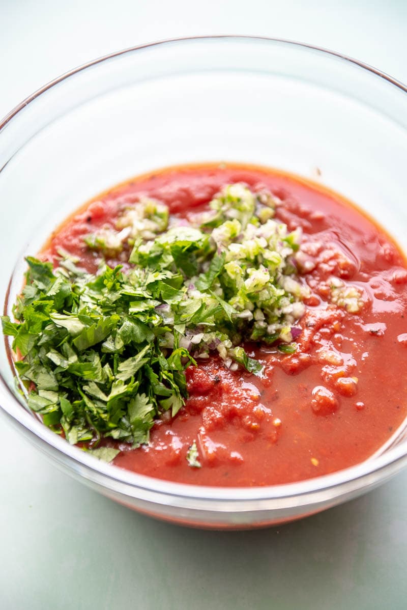 glass bowl filled with canned tomatoes and topped with fresh cilantro and diced onions
