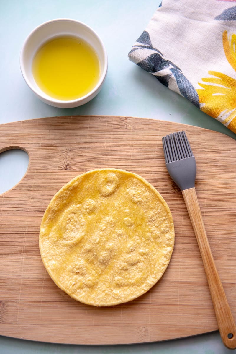 corn tortilla on cutting board with olive oil and brush