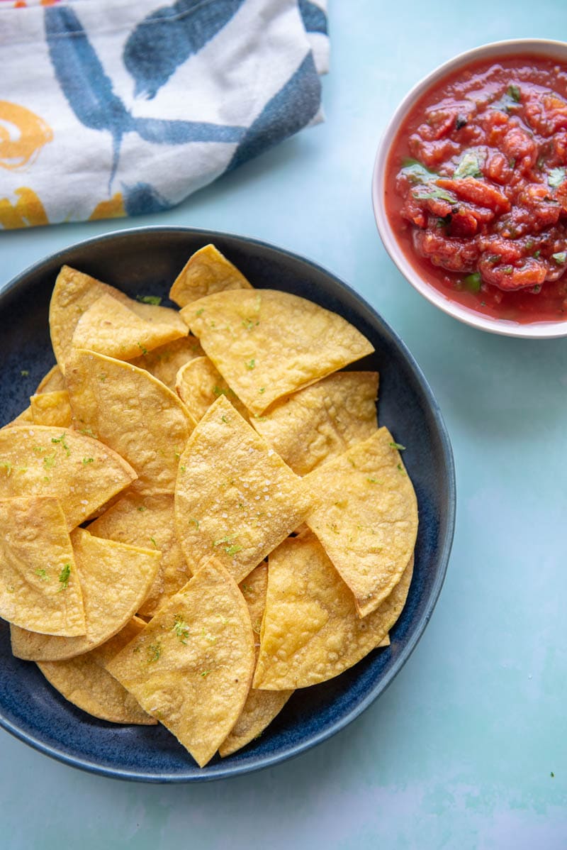 corn tortilla chips on a blue plate next to a pink bowl of salsa