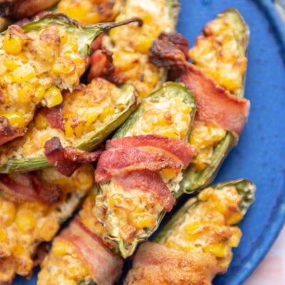 upclose of bacon wrapped jalapeños filled with corn on bright blue plate