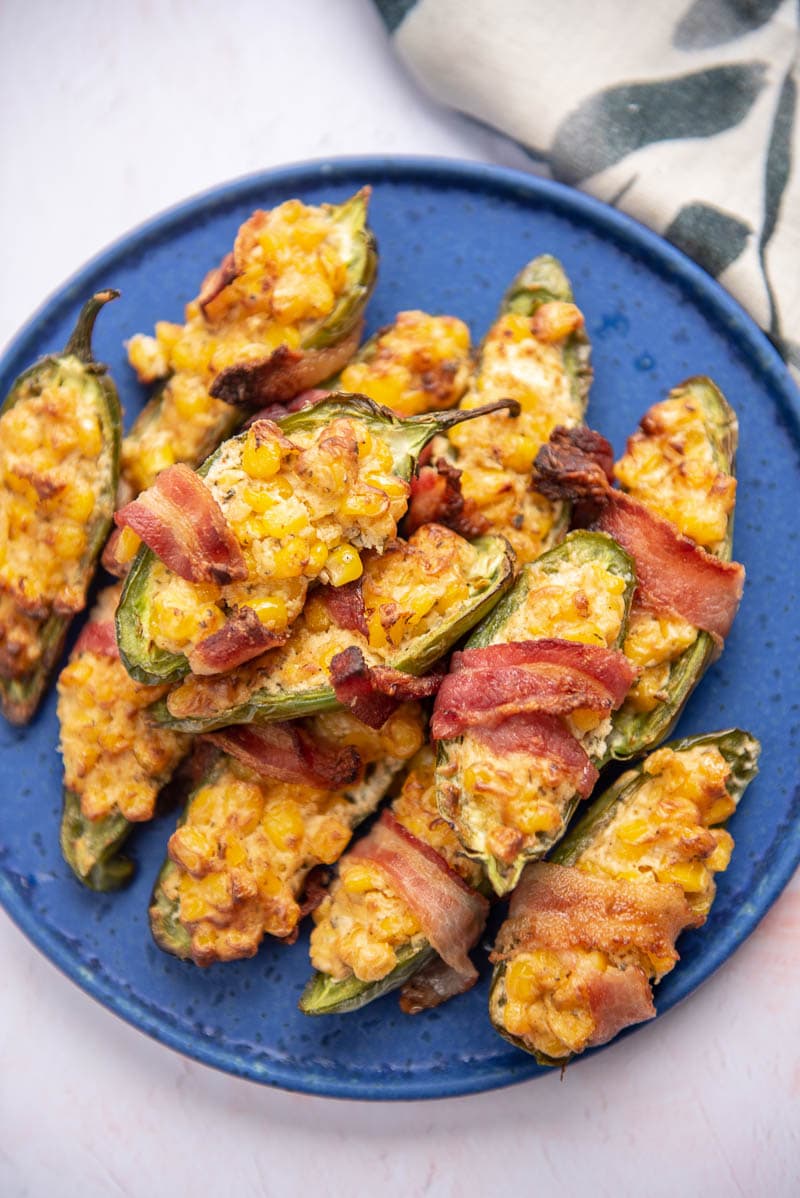 corn filled and bacon wrapped jalapeño poppers piled on a bright blue plate