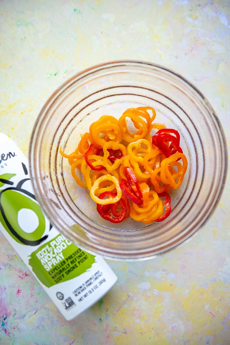 bowl with cut up orange and red peppers next to bottle of avocado oil spray
