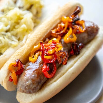 bratwurst in bun topped with peppers on a gray plate
