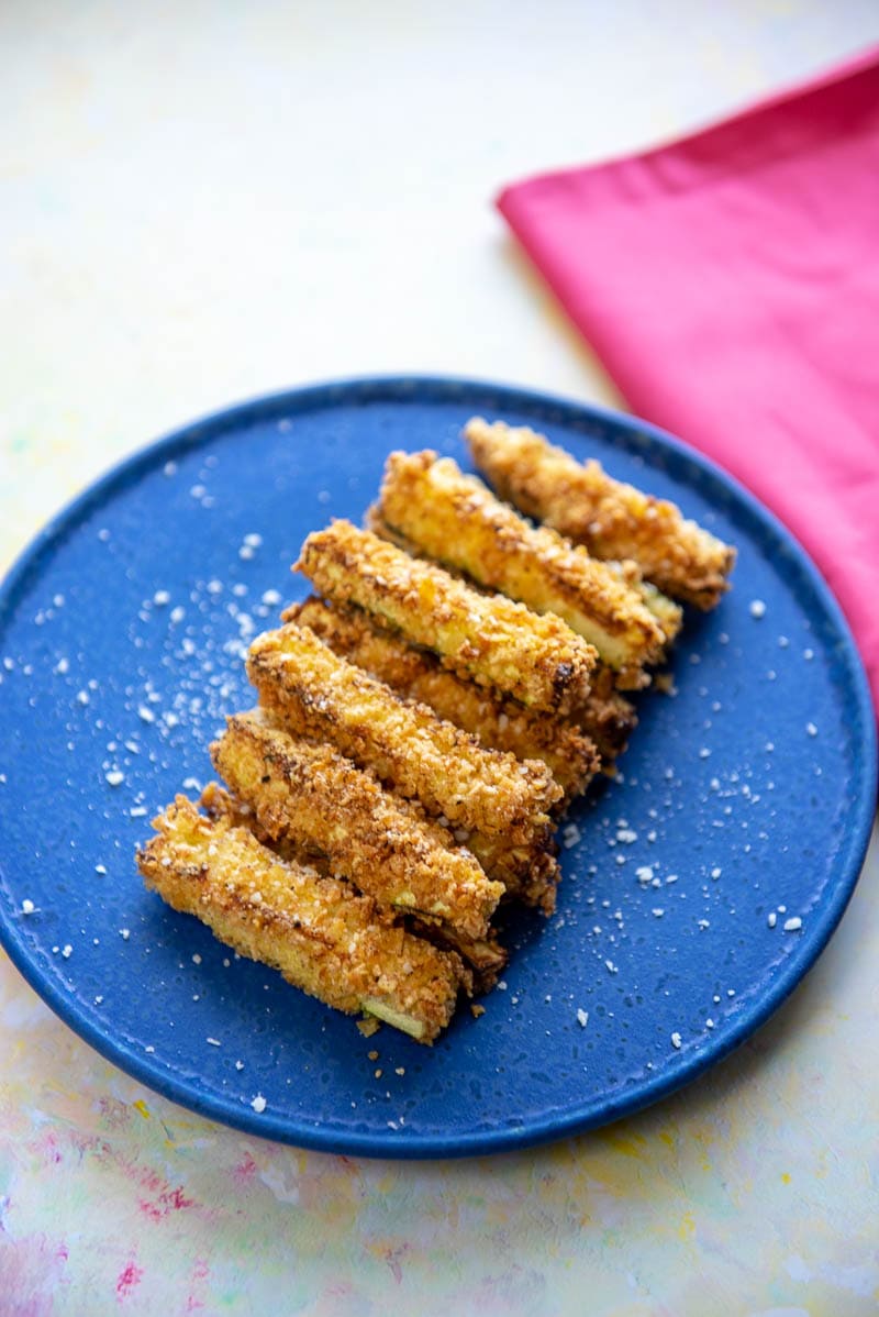 air fryer zucchini fries lined up in two layers on bright blue plate