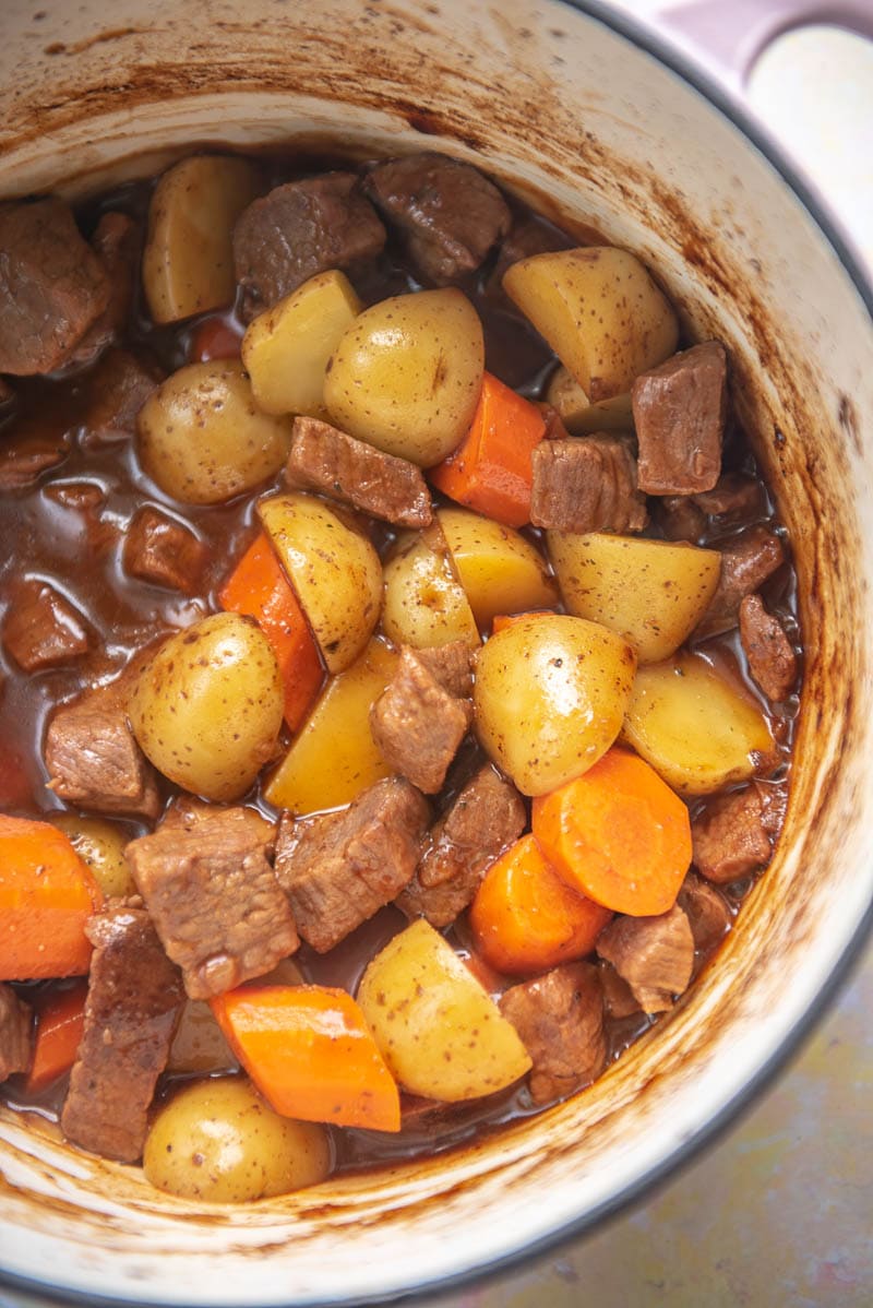 dutch oven filled with cooked beef chunks, carrots and halved potatoes with a gravy
