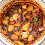 dutch oven pan filled with cooked beef stew with carrots potatoes and parsley