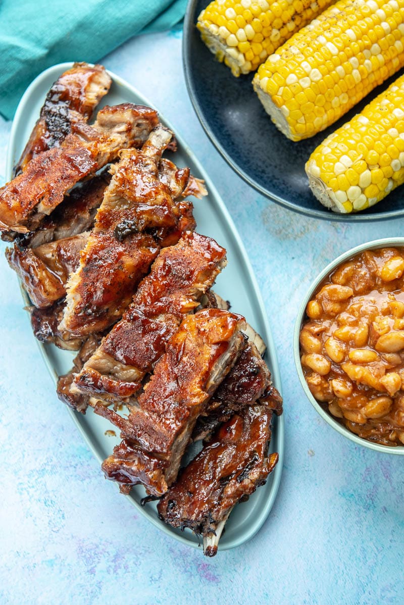 table set with platter of ribs, bowl of beans and corn on the cob