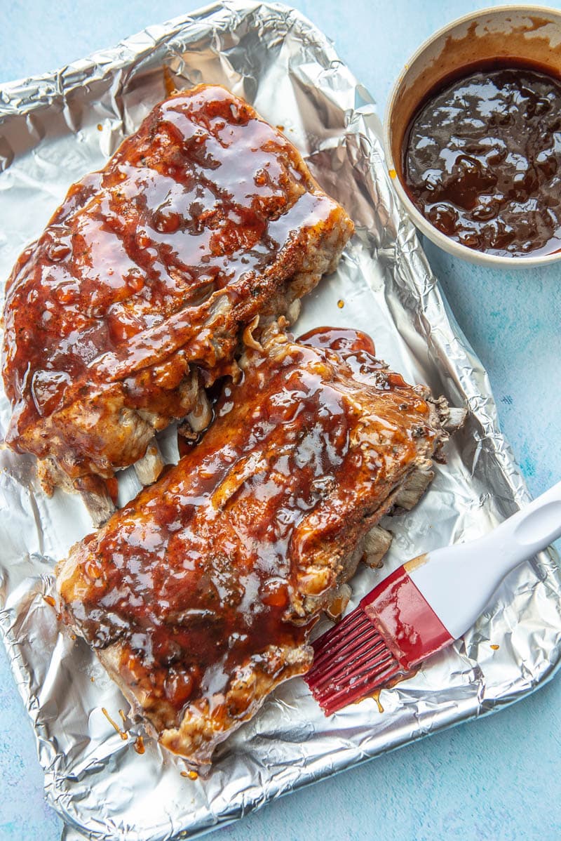 cooked ribs on baking sheet topped with sauce