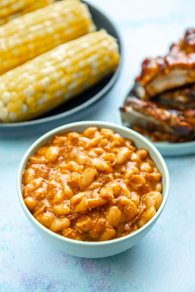 bowl of baked beans next to bowl of corn and platter of ribs