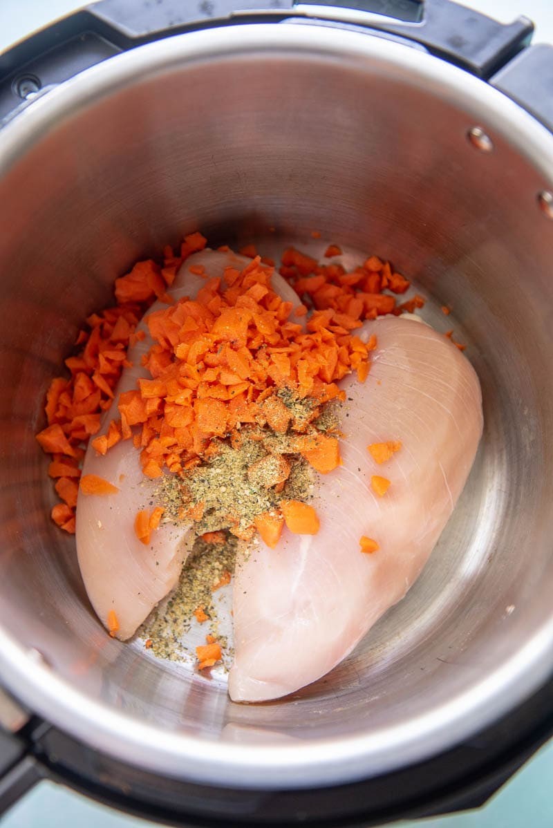 raw chicken with seasonings and chopped carrots in instant pot
