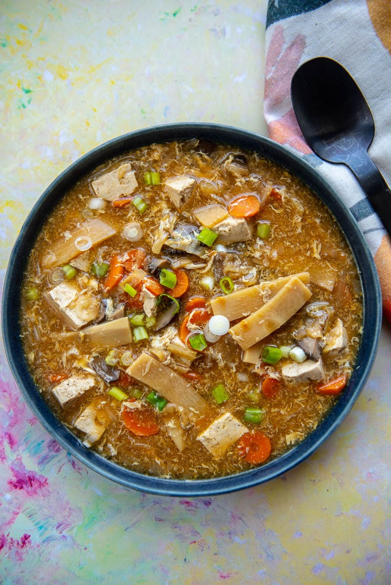 blue pottery bowl filled with hot and sour soup next to black spoon