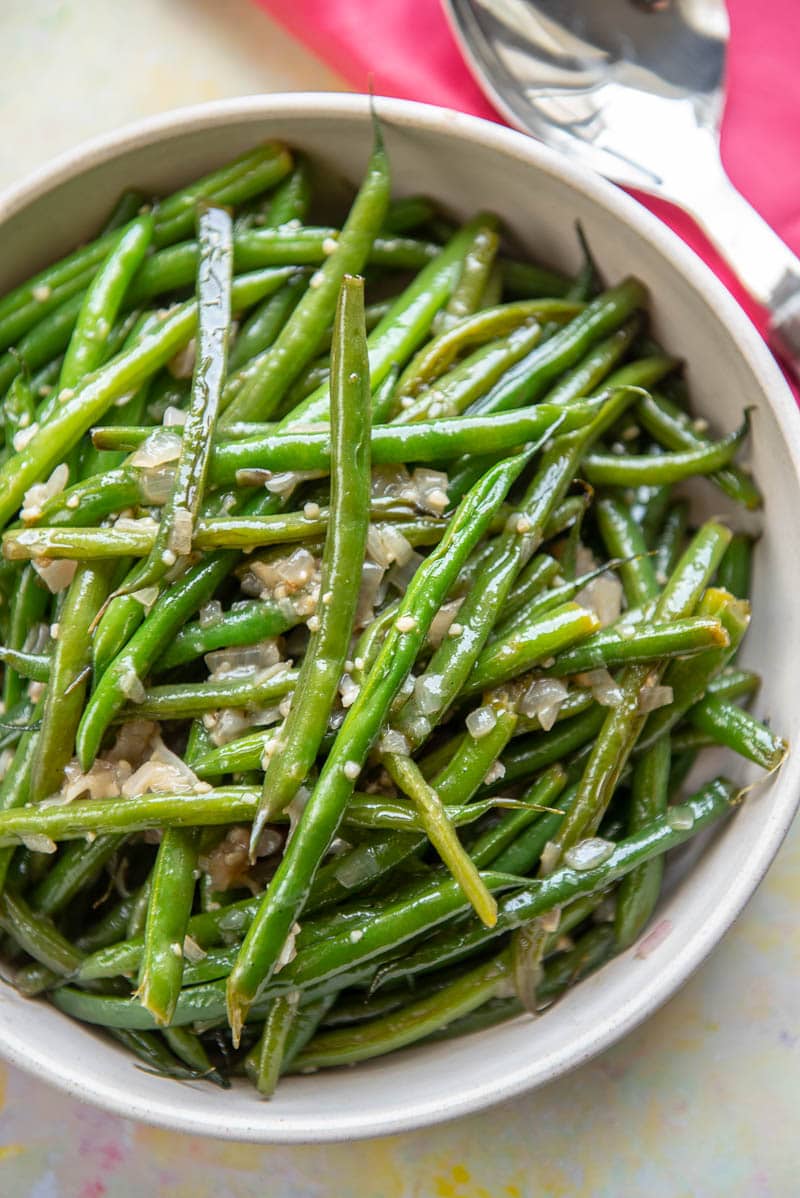 close of up green beans cooked with garlic in a pink serving bowl