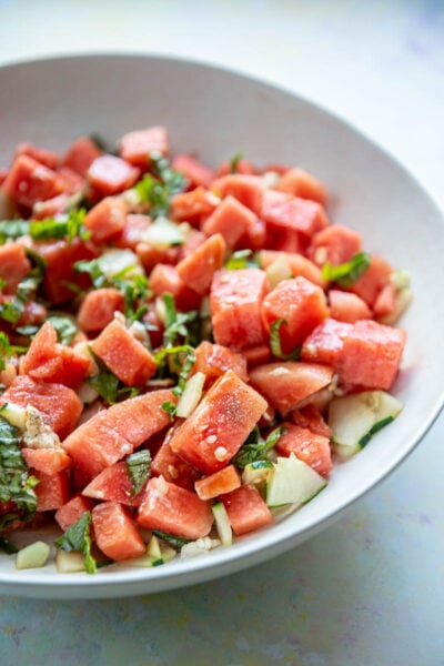 side view of white bowl filled with watermelon salad with cucumber and basil