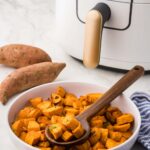 Air Fryer Sweet Potato Cubes served on plate next to whole sweet poatoes and blue and white napkin