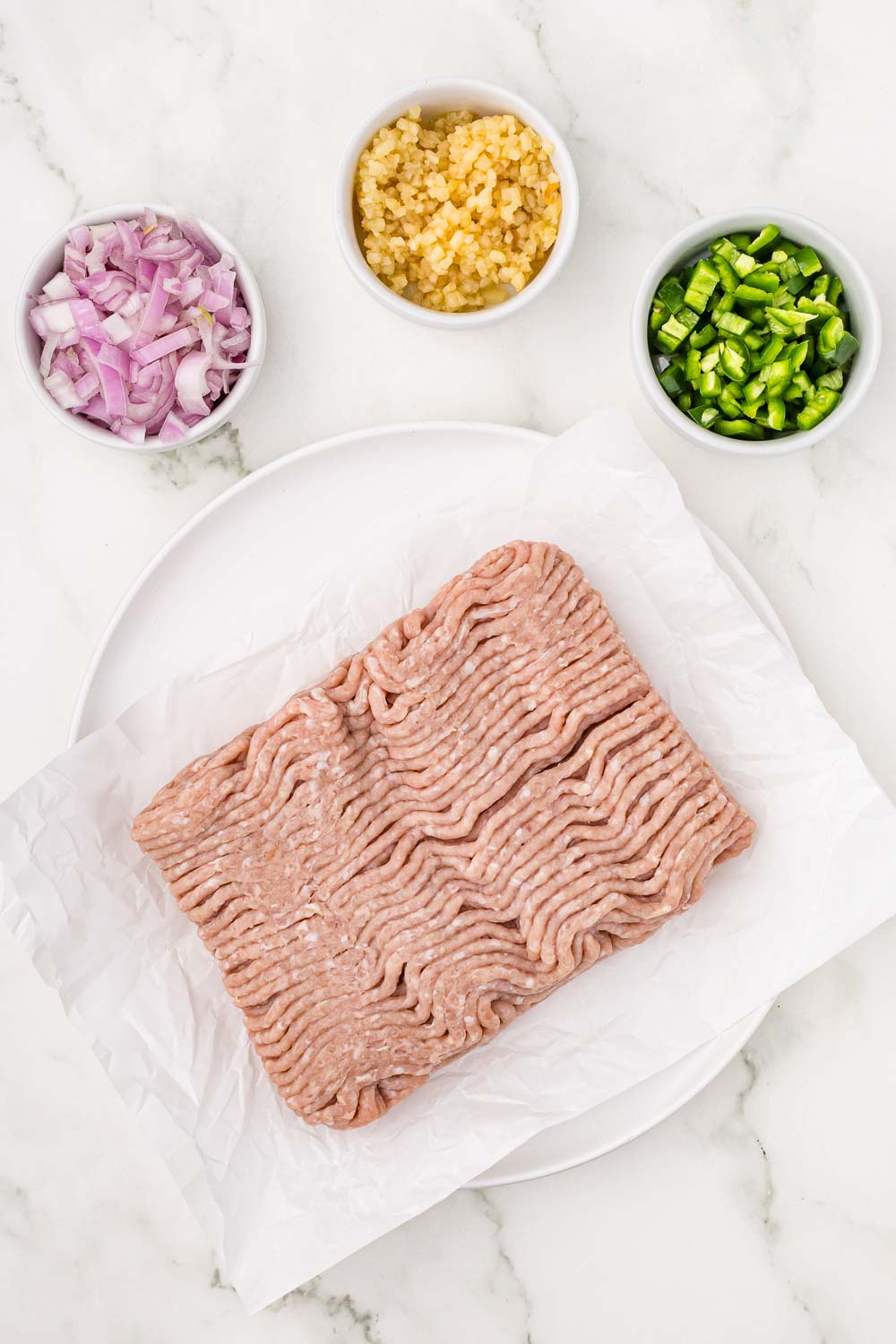 Image of raw ground turkey, chopped red onions, and jalapeno ingredients laid out on a counter.