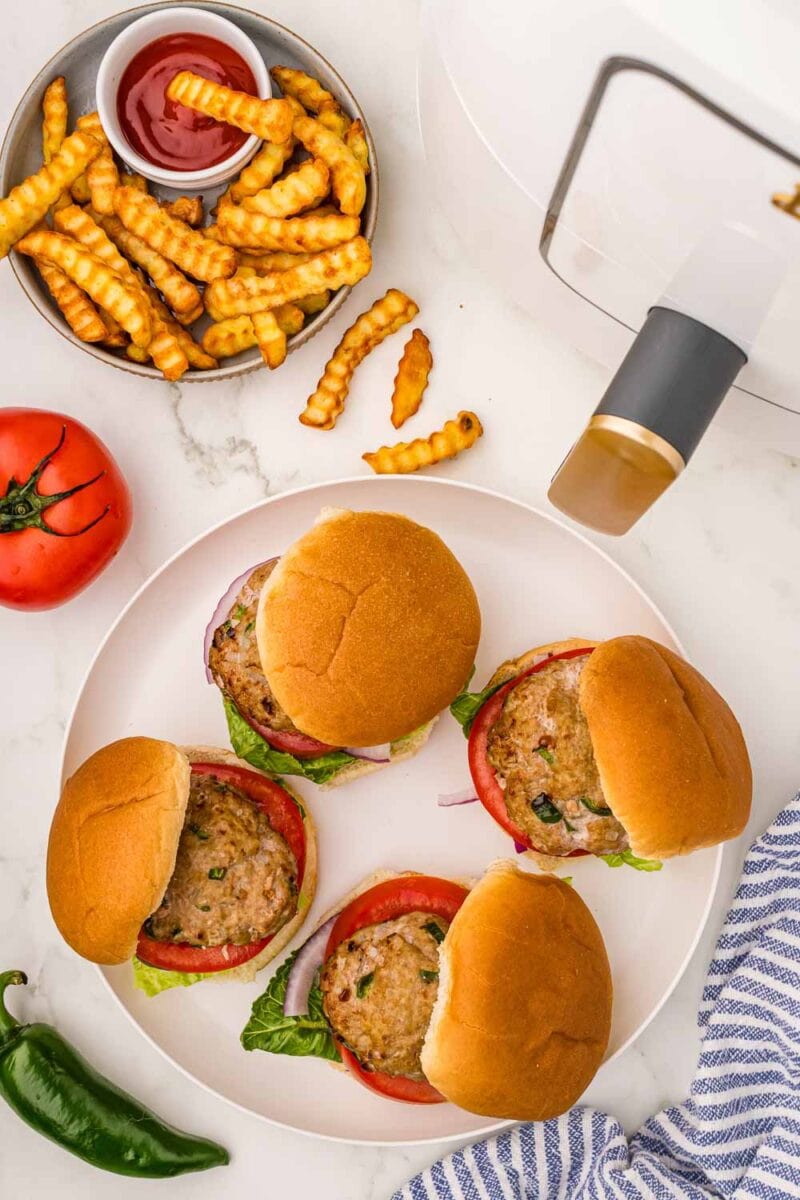 Air Fryer Turkey Burgers served on a bun with tomatoes, red onions, and lettuce, next to large bowl of crinkle cut french fries and ketchup