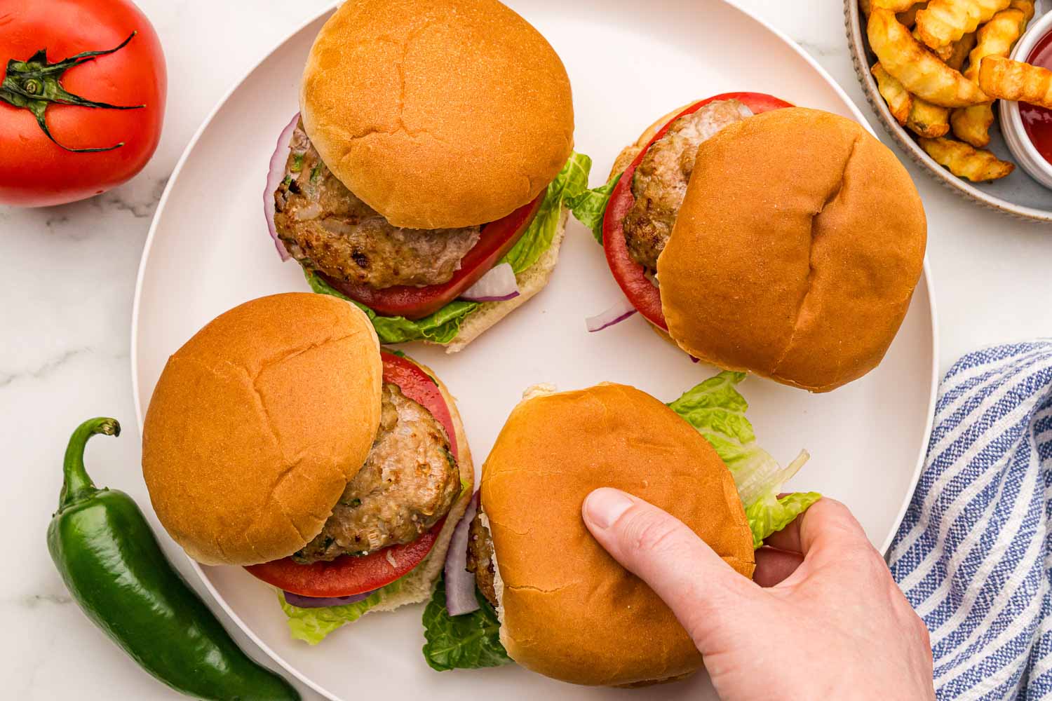 Air Fryer Turkey Burgers served on a bun with tomatoes, red onions, and lettuce, next to large bowl of crinkle cut french fries and ketchup and a jalapeño