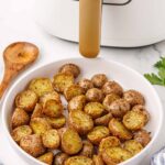 white air fryer in background and white bowl of red crispy potatoes in front