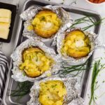 4 baked potatoes in open foil cut open on cookie sheet topped with butter and chives