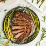 Sliced rib eye steak booked and served on plate with asparagus