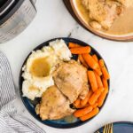 overhead view of plated chicken thighs, carrots, mashed potatoes and gravy next to instant pot and serving bowl of chicken