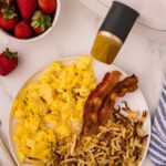 Air Fryer Hashbrowns served with scrambled eggs and 2 slices of bacon next to small bowl strawberries