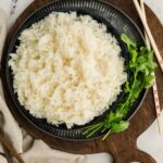 Fluffy Cooked jasmine rice served on black plate with cilantro next to plate for garnishing