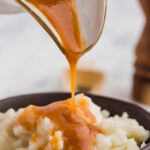 Close up of brown gravy being poured onto bowl of mashed potatoes