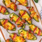 cutting board topped with white parchment and array of stuffed jalapeño poppers