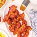 cooked bacon on a white plate next to white air fryer