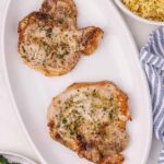 two cooked herbed pork chops on a white platter
