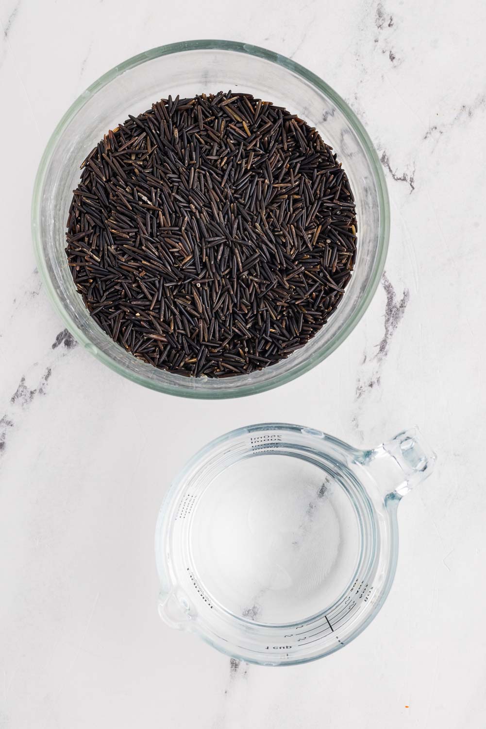 Uncooked wild rice in bowl next to measuring cup with water
