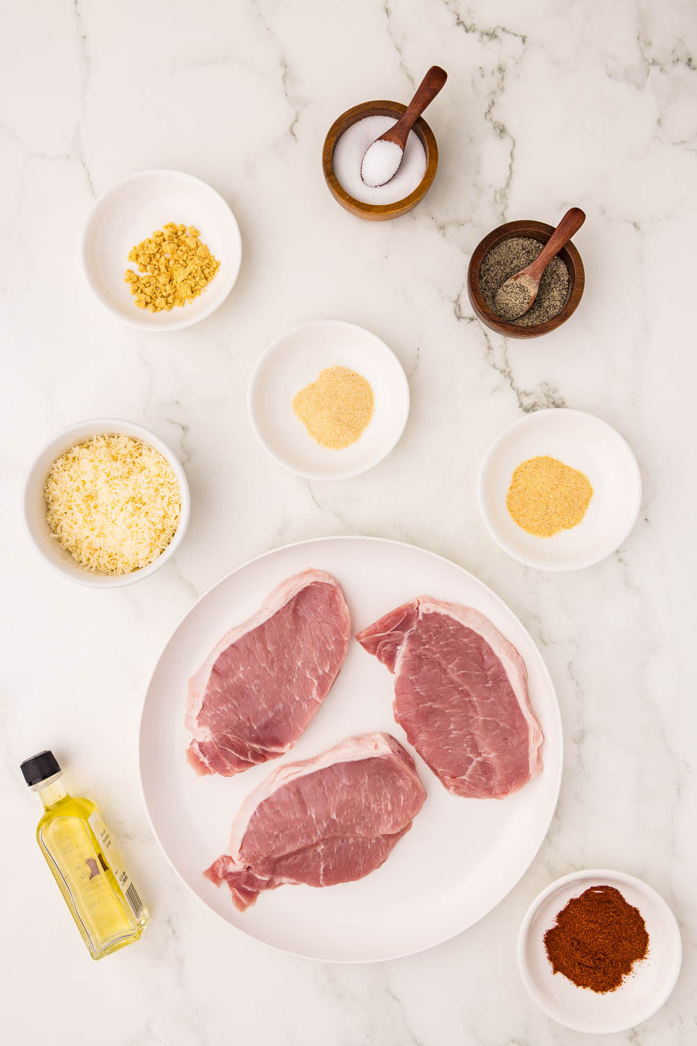 Ingredients like boneless pork chops (about ¾ - 1 inch thick each) 1 tablespoon olive oil ½ cup grated parmesan cheese 1 tablespoon smoked paprika 1 teaspoon garlic powder 1 teaspoon onion powder 1 teaspoon dried mustard powder ½ teaspoon salt ¼ teaspoon pepper laid out on counter