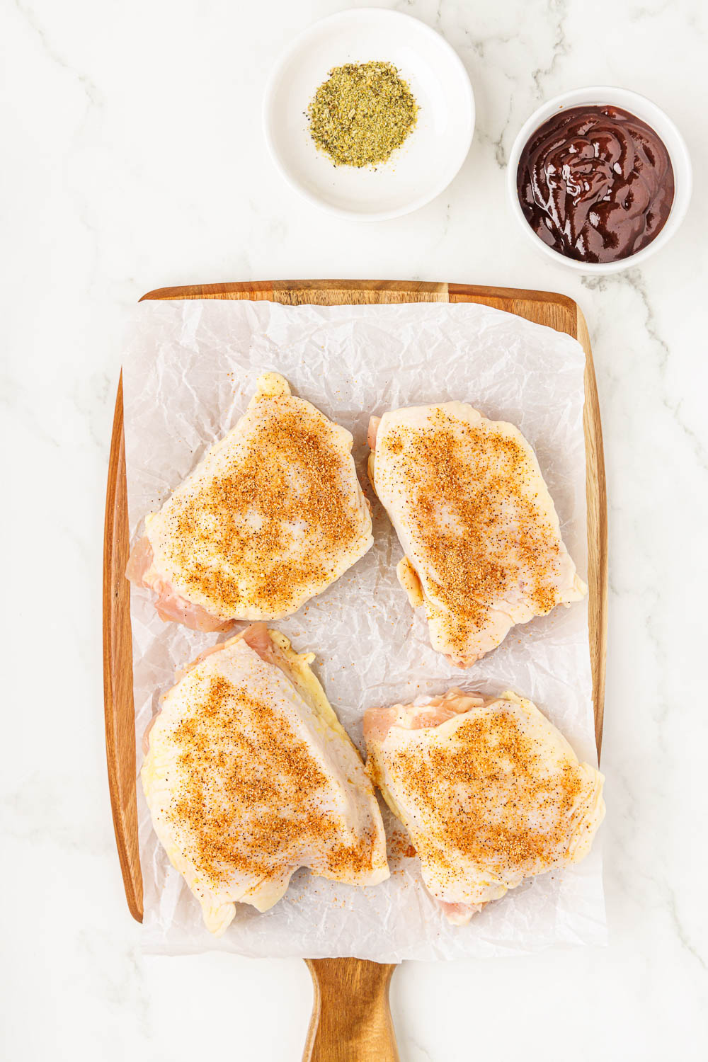 4 bbq chicken thighs seasoned on cutting board over parchment paper