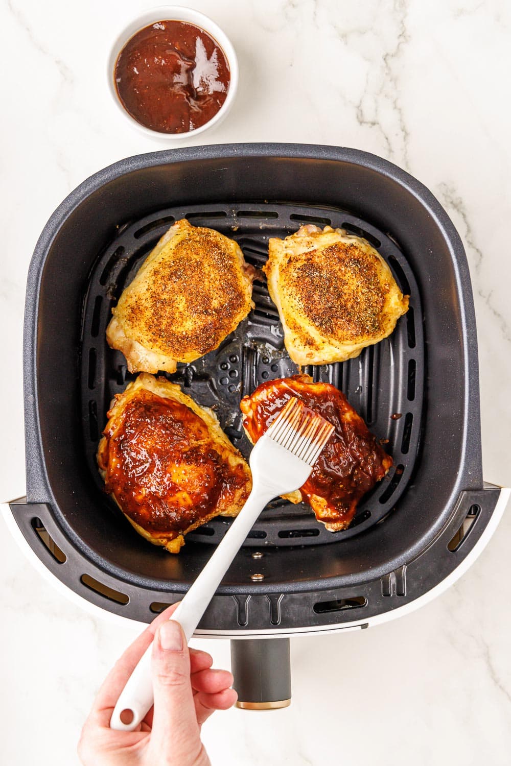 4 chicken thighs in air fryer being brushed with BBQ