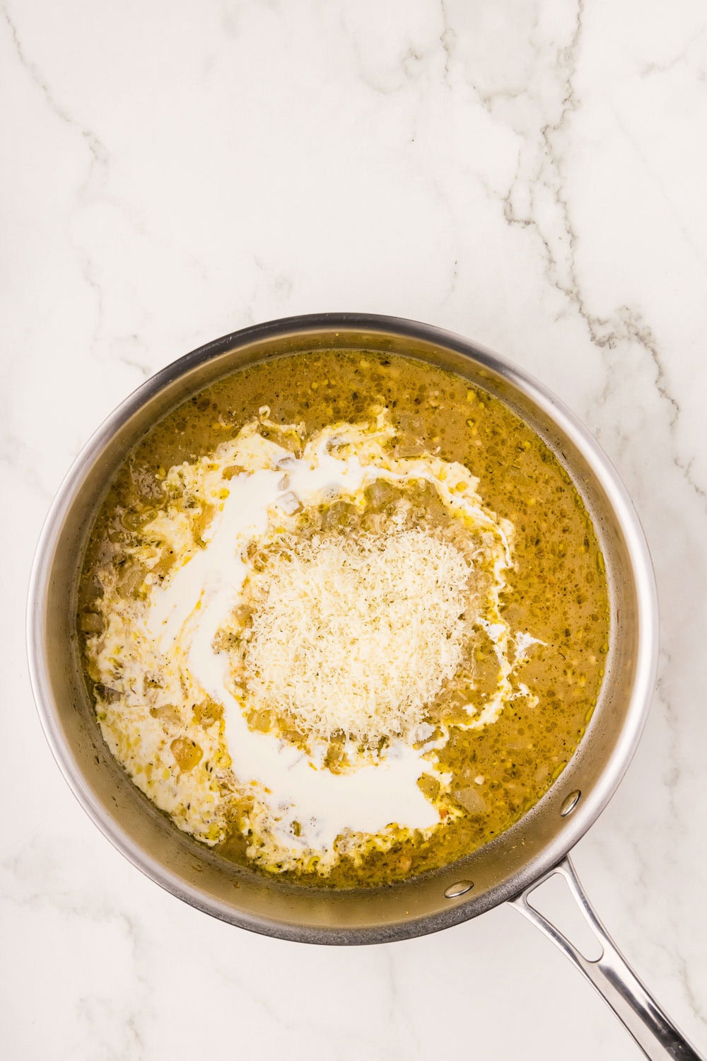 Lemon juice and chicken broth in a pan with heavy cream and cheese being brought to a a simmer