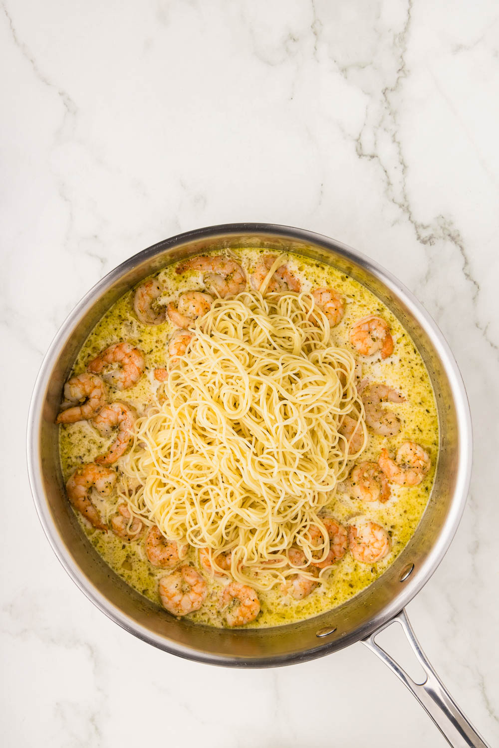 Lemon juice and chicken broth in a pan with heavy cream and cheese being brought to a a simmer in a skillet with shrimp cooking with cooked with angel hair pasta inside