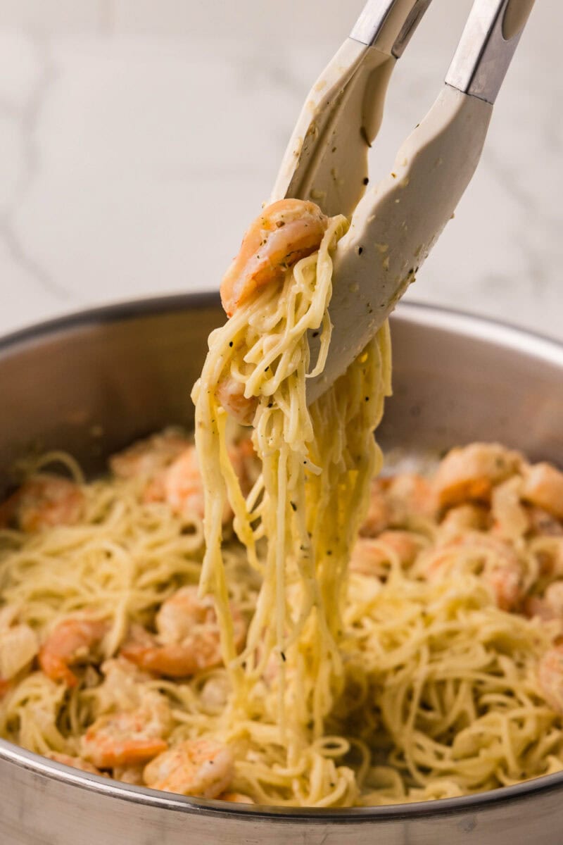 Cooked Lemon Garlic Shrimp Pasta in a skillet being picked up with tongs