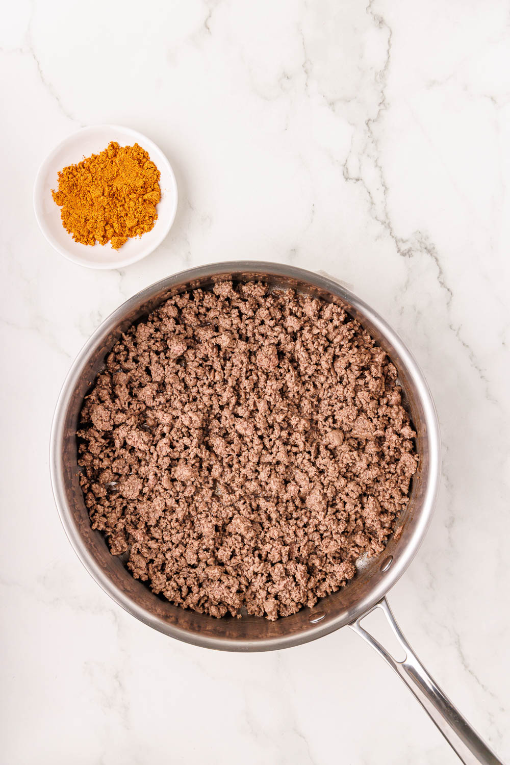 Taco meat ground beef in and next to seasoning in small dish