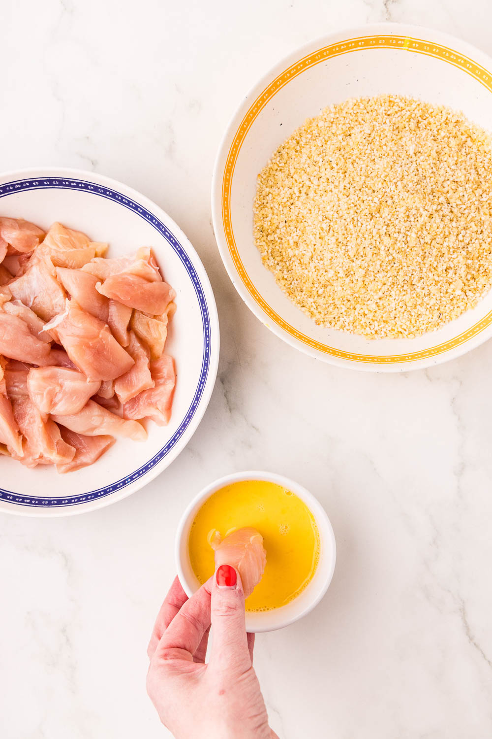 Raw chicken, panko crumbs, and beaten egg on counter ready to prepare recipe chicken dipping into egg