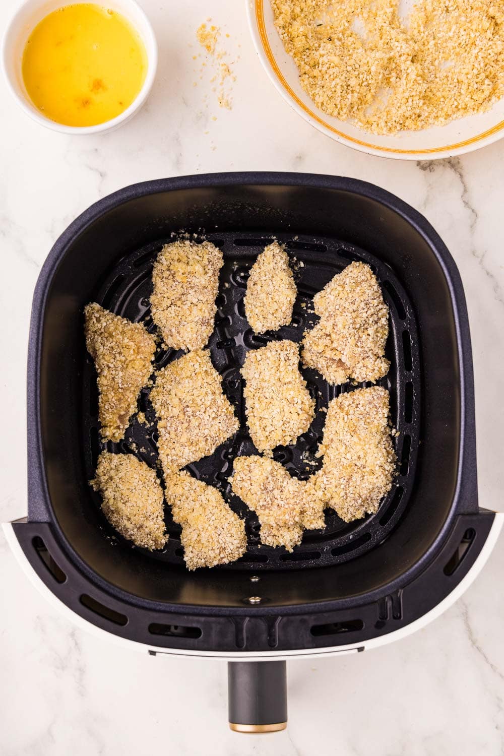 Panko crumbs covered chicken tenders going into air fryer to be cooked