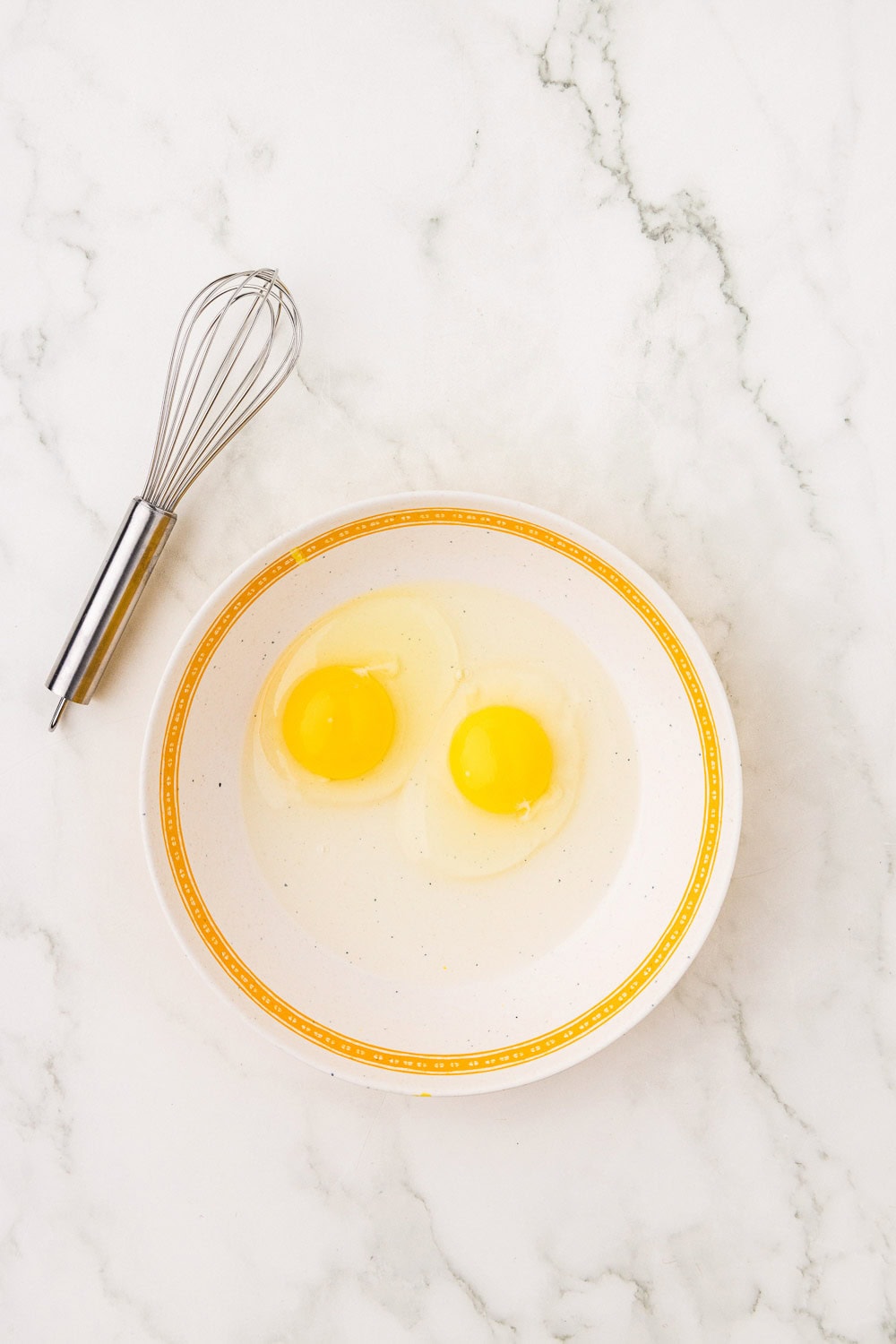 2 eggs in plate next to whisk