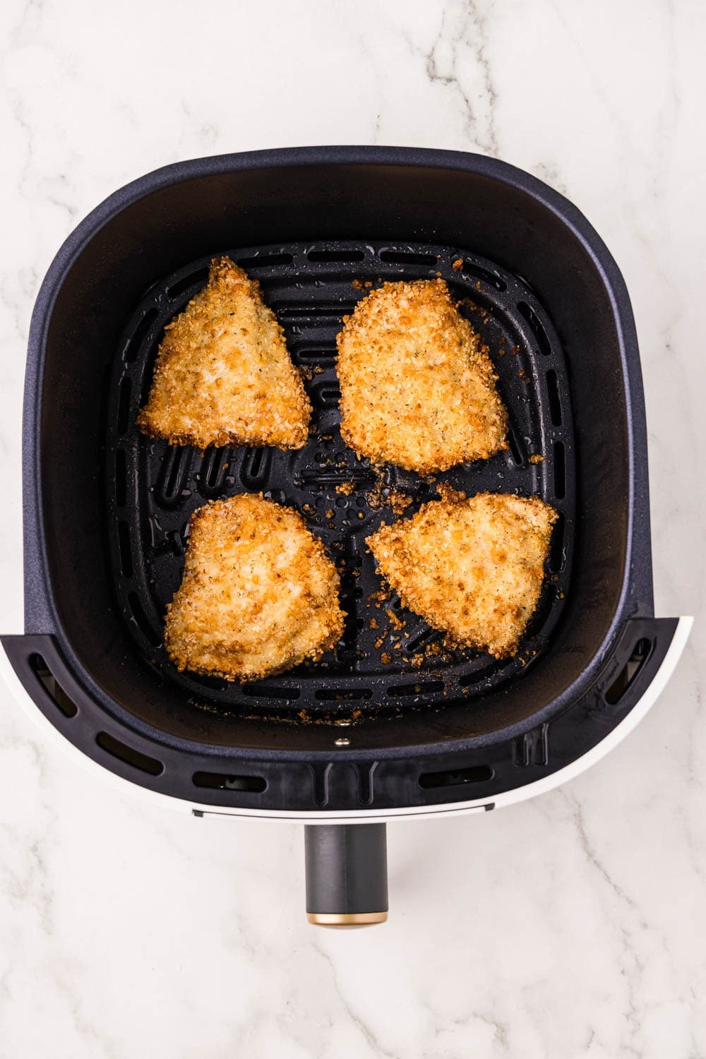 Air fryer basket with cooking spray with cooked chicken in basket it a single layer not overlapping