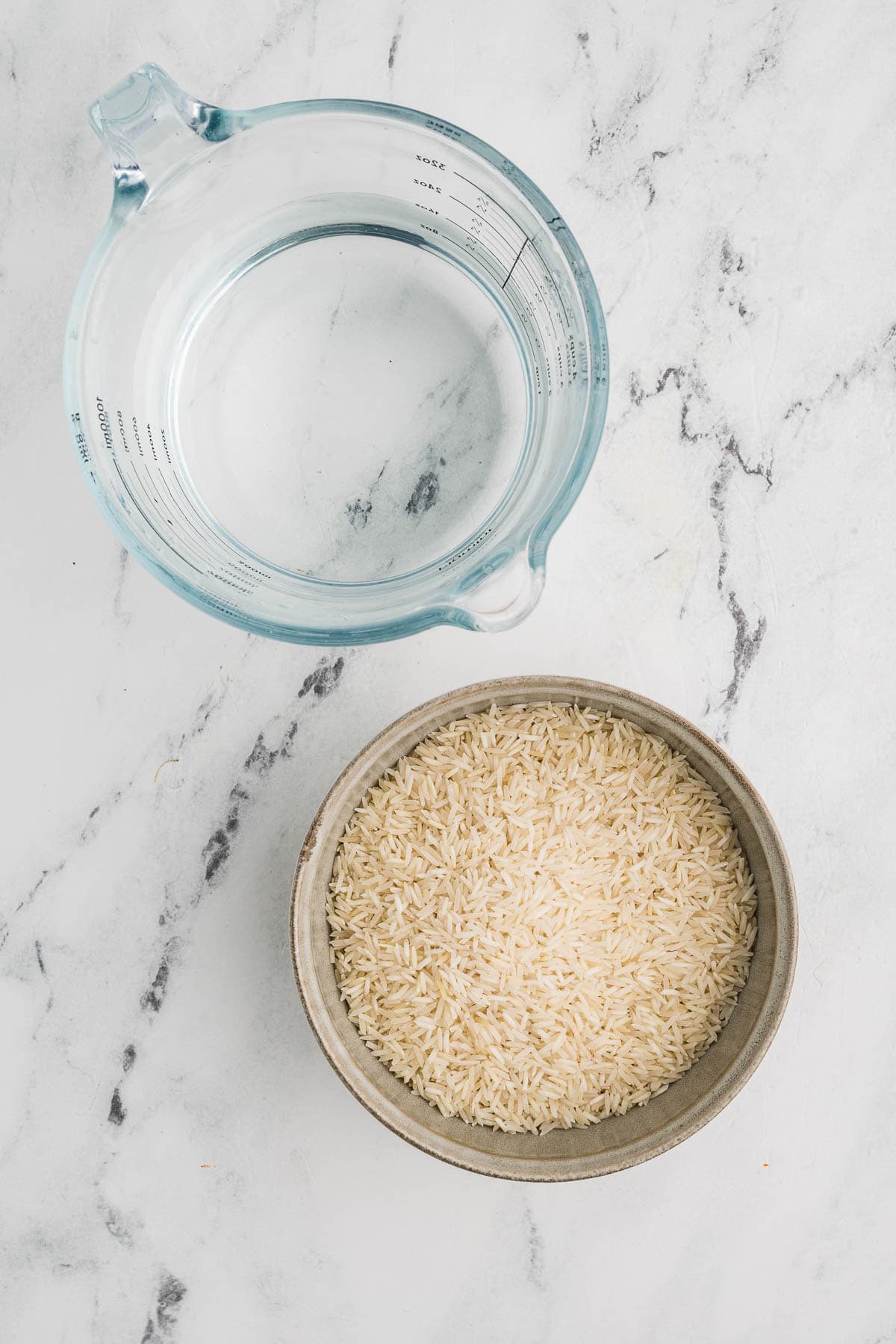 Bowl with uncooked rice next to measuring cup of water