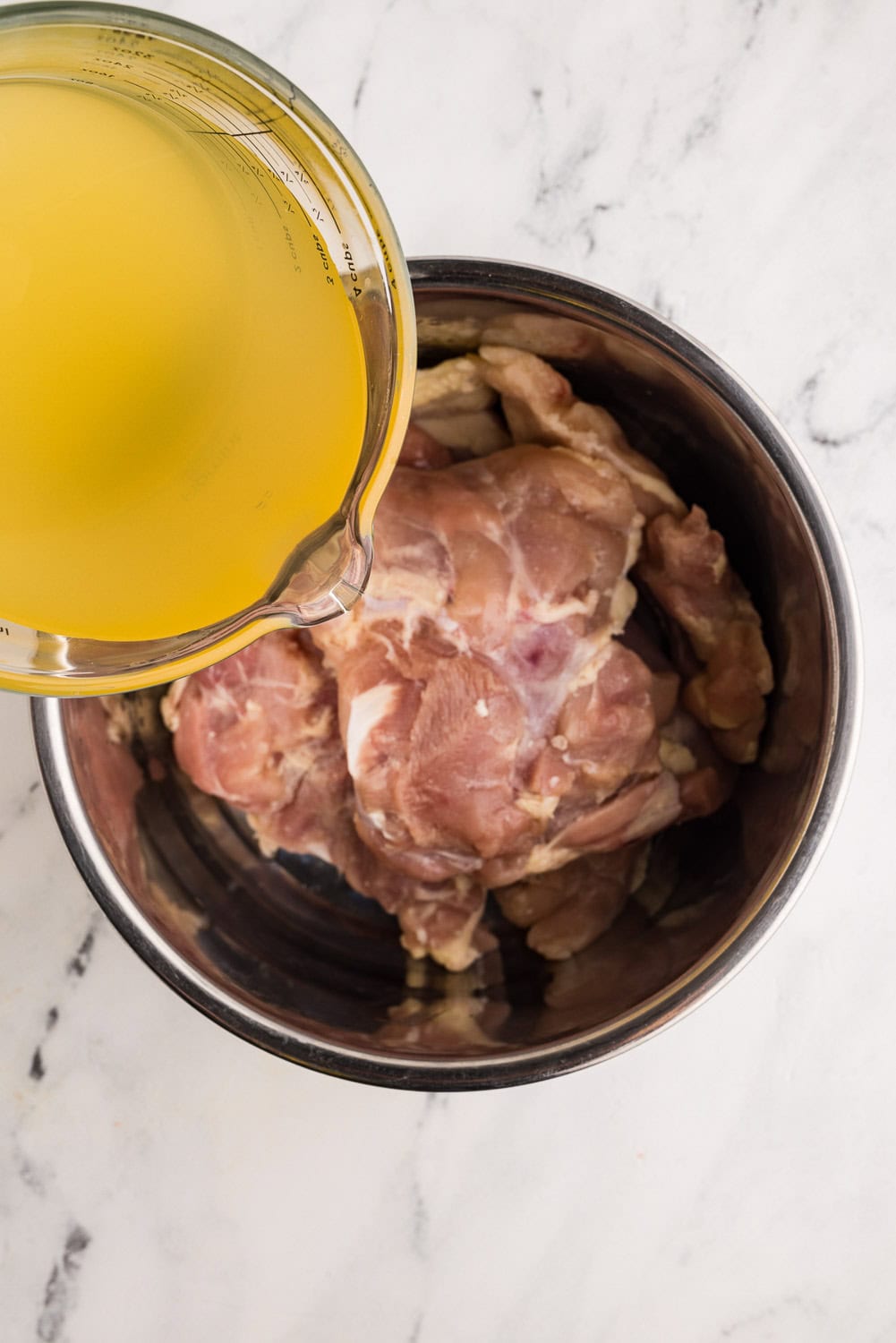 pouring measuring cup of broth over chicken thighs in instant pot