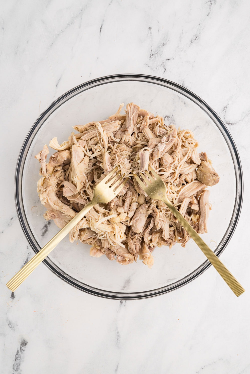 shredded chicken with two forks in glass bowl