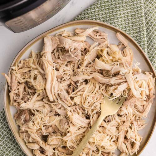 shredded chicken on white plate with gold fork next to instant pot
