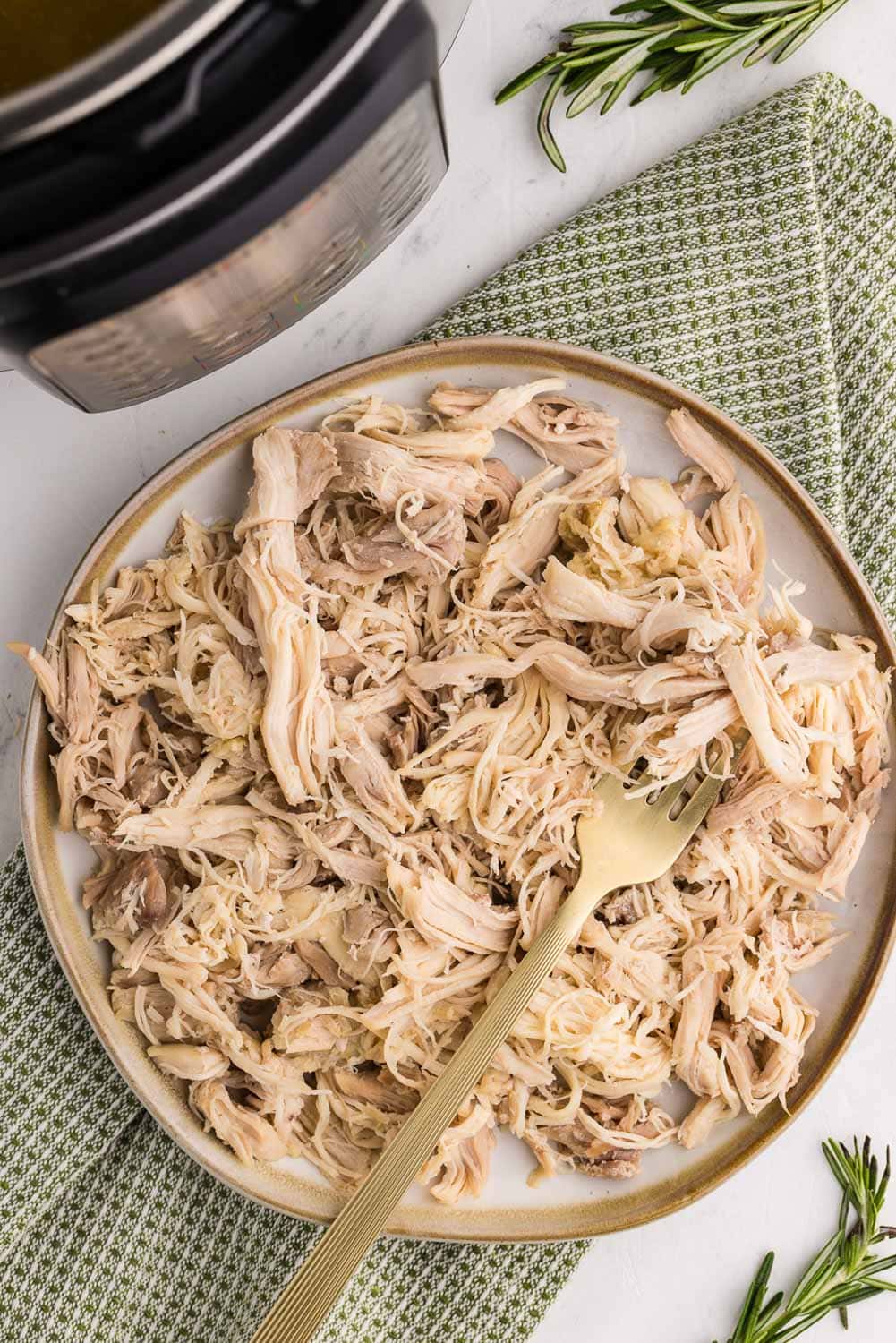 shredded chicken on white plate with gold fork next to instant pot
